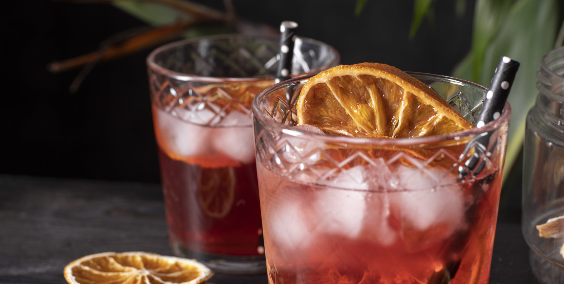 Two cocktails with ice and dried orange slices in cut glasses.