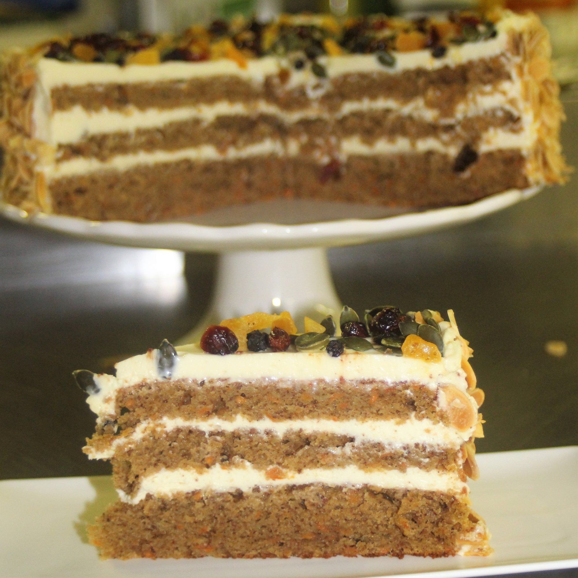 Slice of fruit cake with cream and nuts on a white plate.