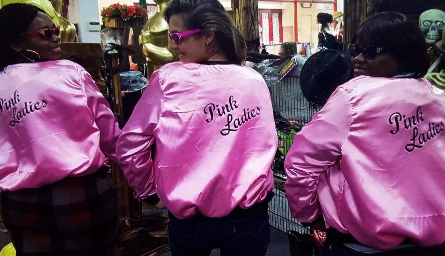 Three people in pink jackets with 'Pink Ladies' on display
