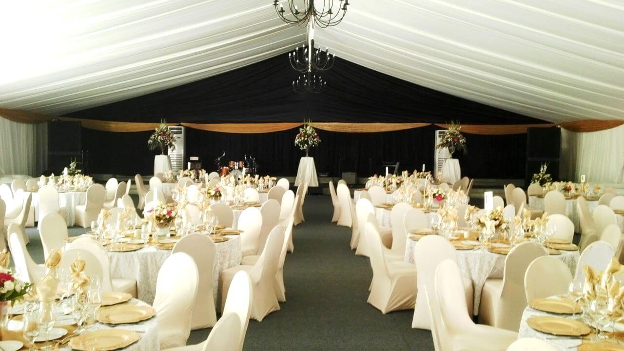 Elegant event setup with round tables, floral decor, and black backdrop.