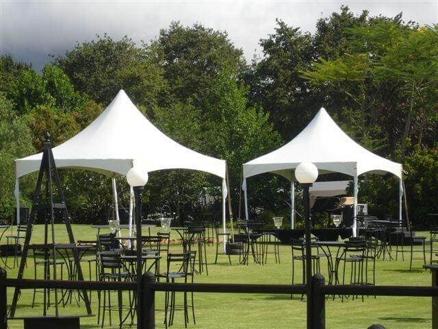 Two white tents on green grass with black tables and chairs.
