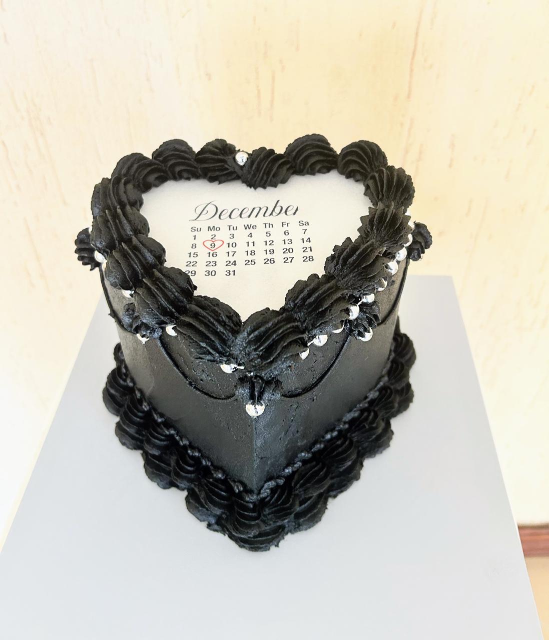 Heart-shaped cake with black icing and calendar on top