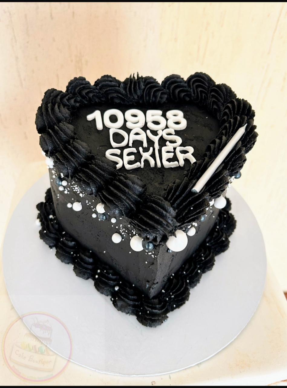 Heart-shaped black cake with white lettering and rosettes