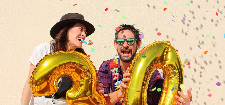 Two people celebrating with large gold number balloons and confetti