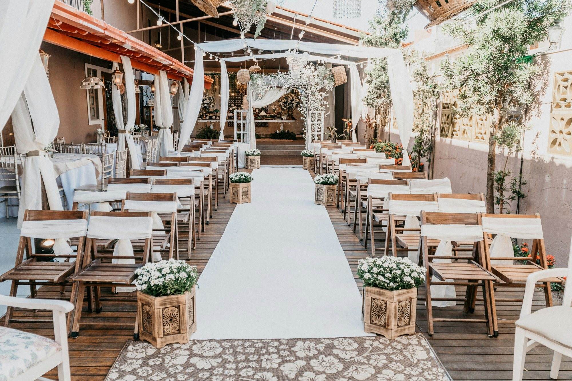 Wooden chairs arranged along a white aisle in an outdoor wedding setting