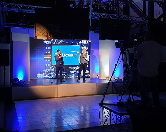 Two comedians on stage with a backdrop and blue lighting.