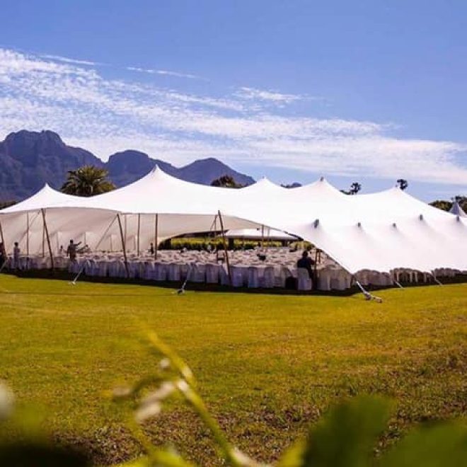 Large stretch tent setup on a grassy area with mountains in the background