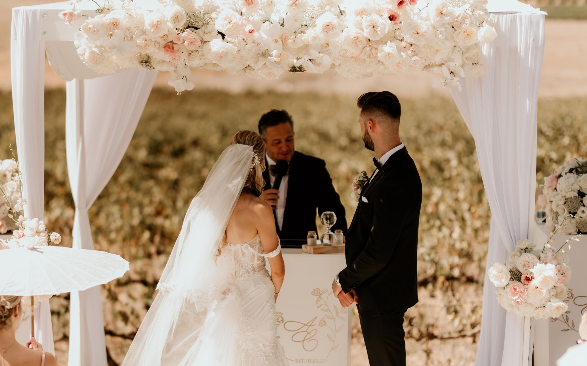 Couple at outdoor wedding ceremony under floral arch
