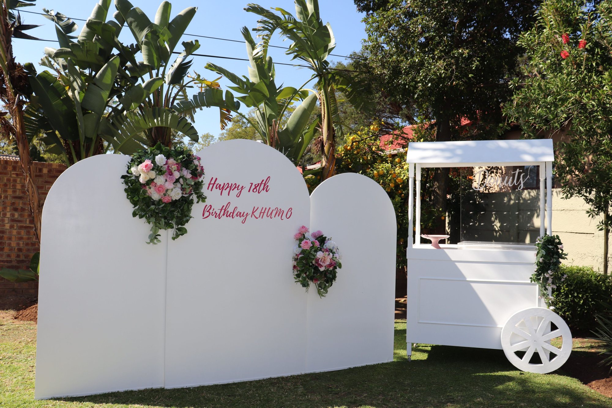 White backdrop with flowers and a decorations cart for a birthday celebration