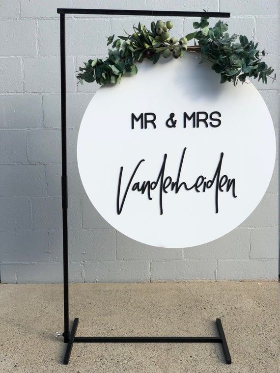 White circular welcome sign with greenery and the names 'Mr & Mrs VandenHeiden'