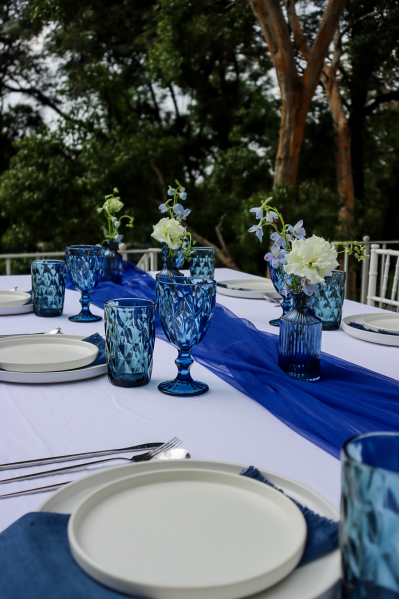 Blue glassware and floral centerpieces on a white table setting