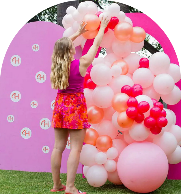 A person adjusting a colorful organic balloon installation against a backdrop