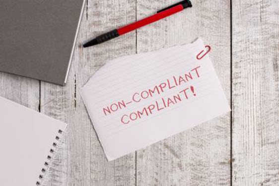 Handwritten note saying 'NON-COMPLIANT' on wooden surface.