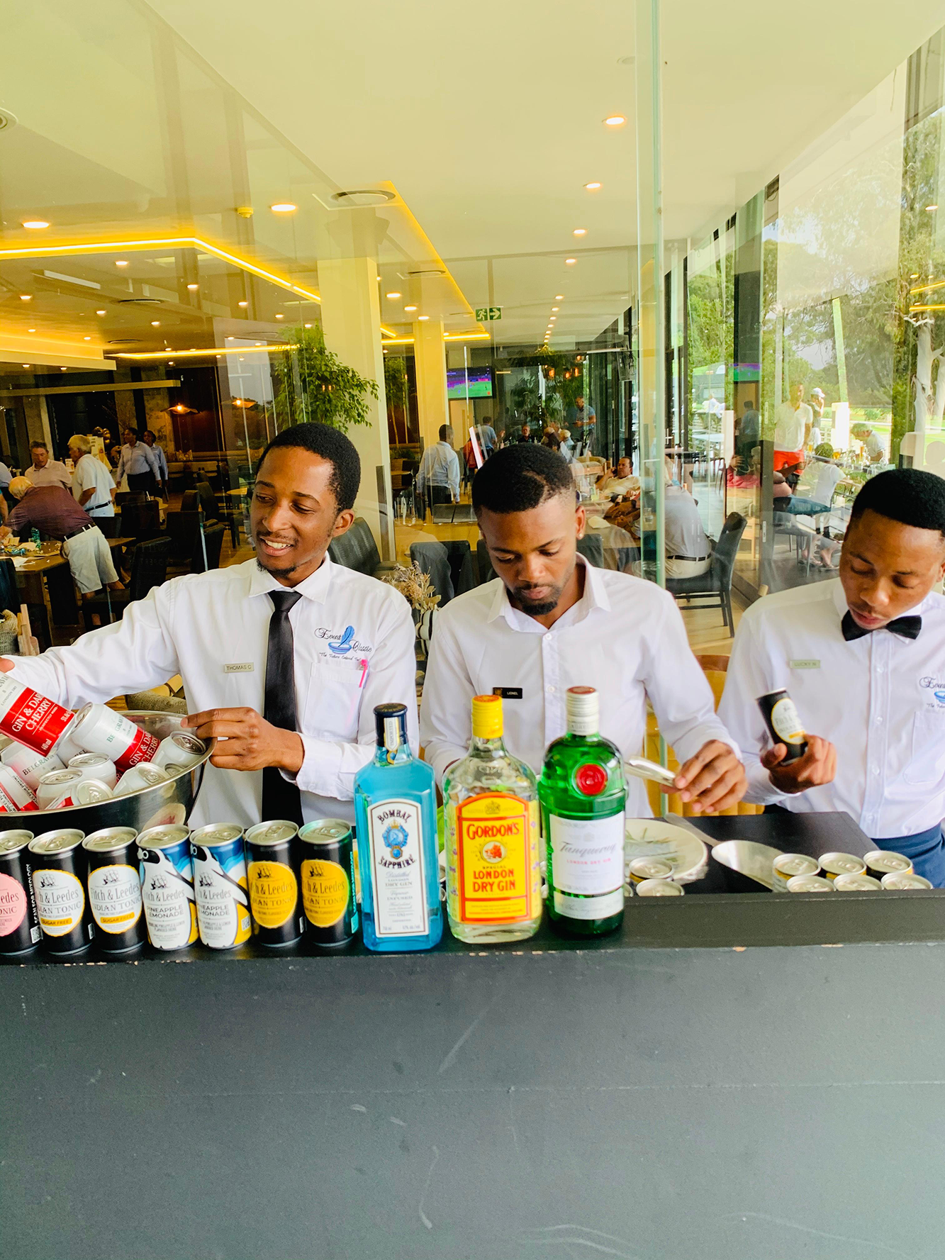 Three bartenders mixing drinks behind a bar with various liquor bottles