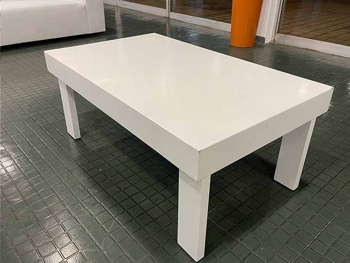 White coffee table with four legs on a green tiled floor.