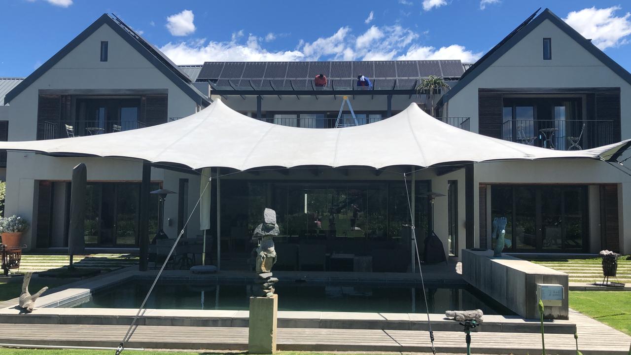 Wide outdoor canopy set up in a backyard with a pool.
