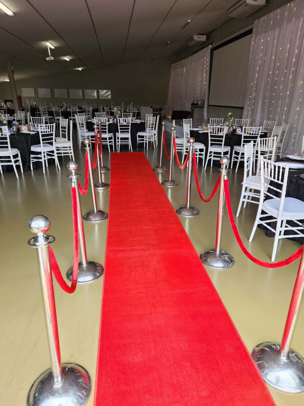 Red carpet entrance with stanchions and chairs in a decorated venue