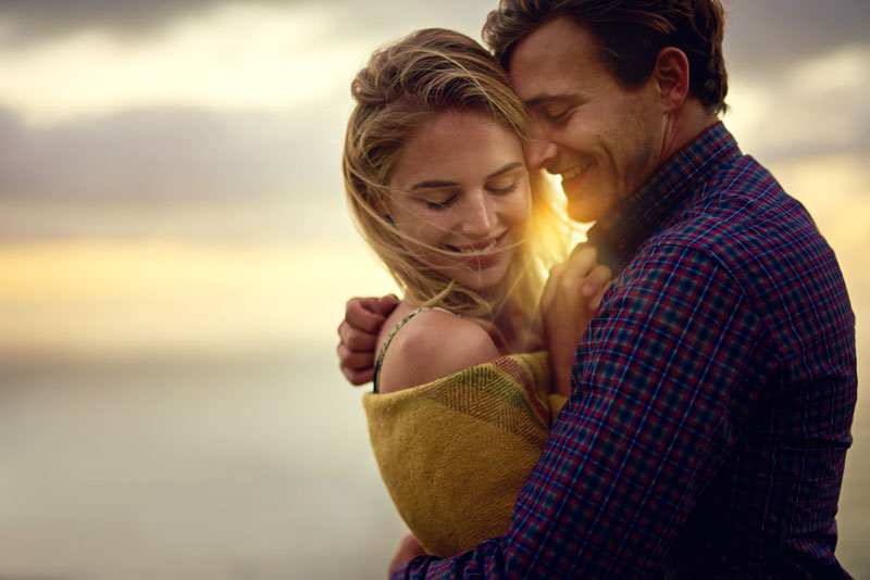 A couple embracing with a sunset backdrop.