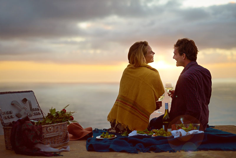 Couple enjoying a picnic by the ocean at sunset.