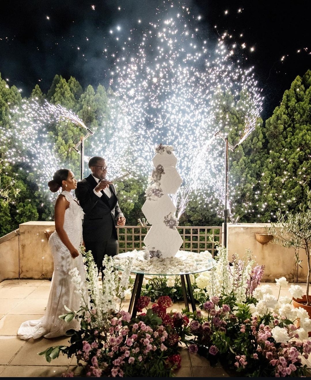 Couple at wedding with fireworks and flowers around a cake