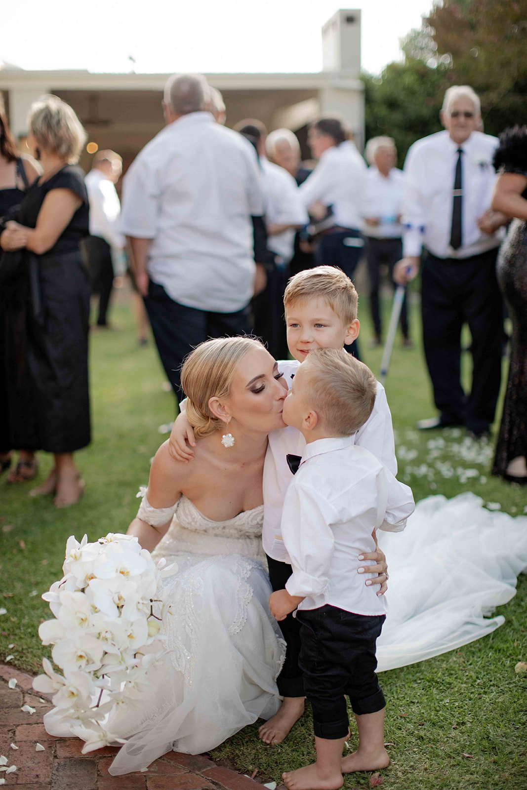 Bride kissing two children in a garden setting.