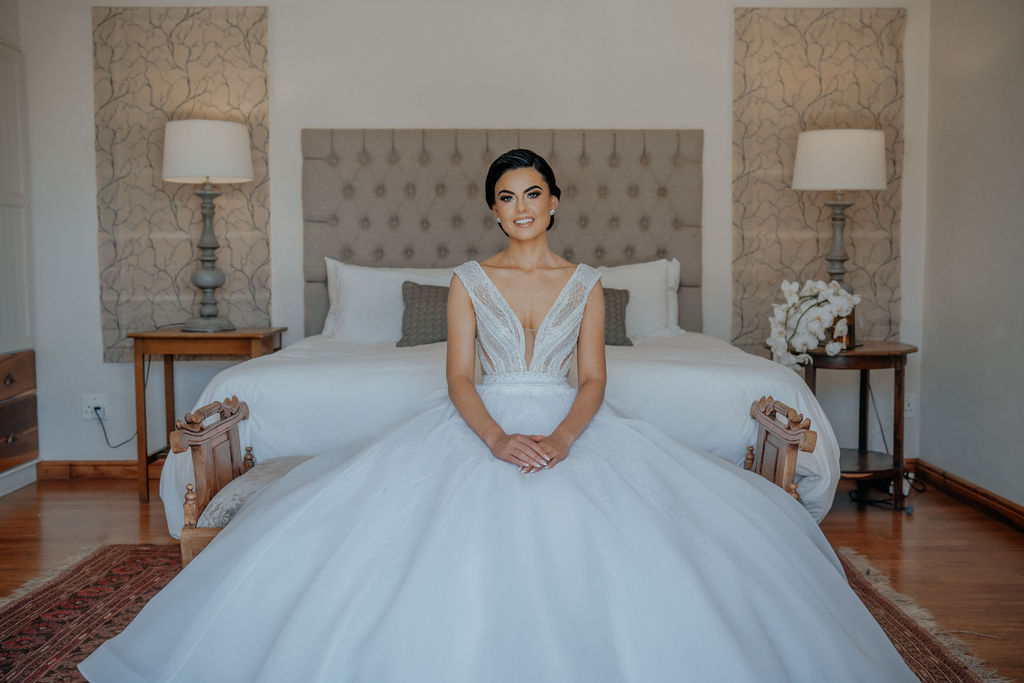 Bride in white dress seated in a decoratively styled room.