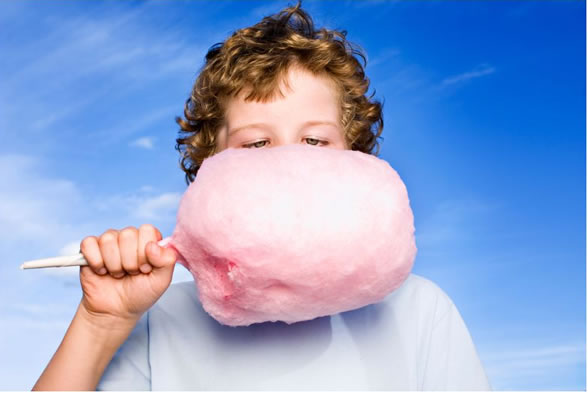 Child holding large pink cotton candy against a blue sky.