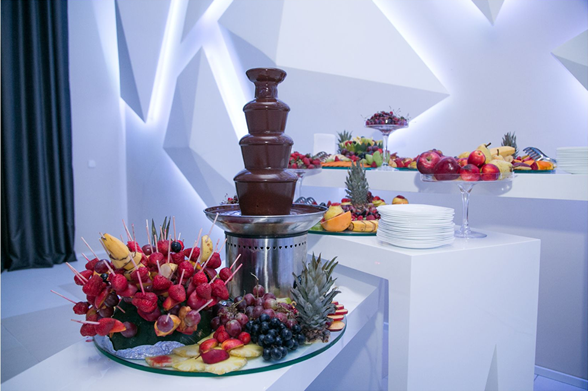 Chocolate fountain surrounded by fresh fruit displays.