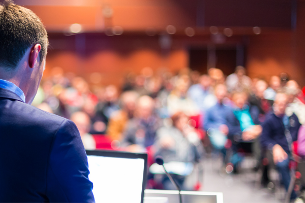 Man presenting at a corporate event with audience in the background