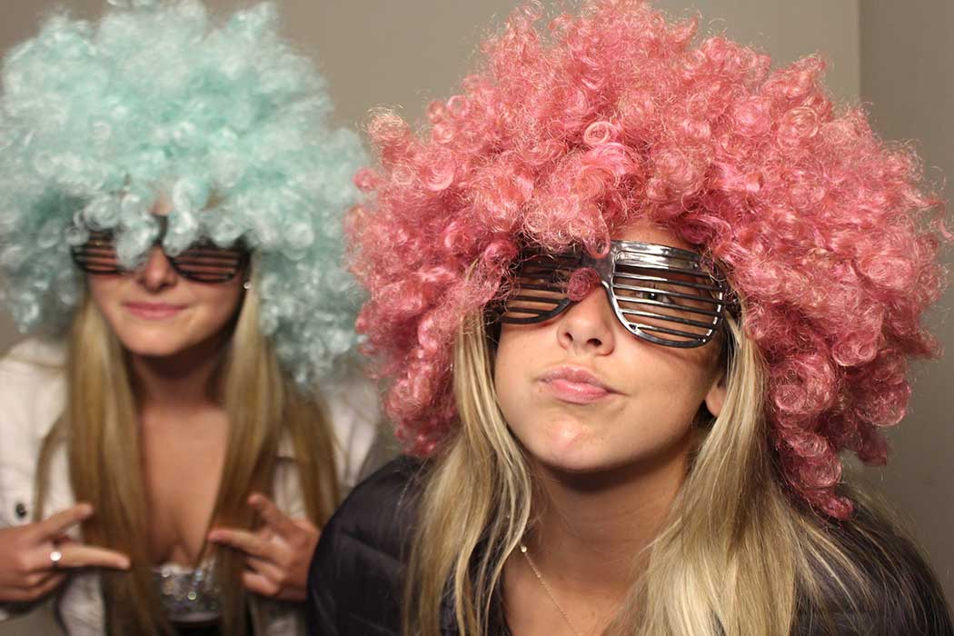 Two women in colorful wigs and sunglasses posing at a photo booth
