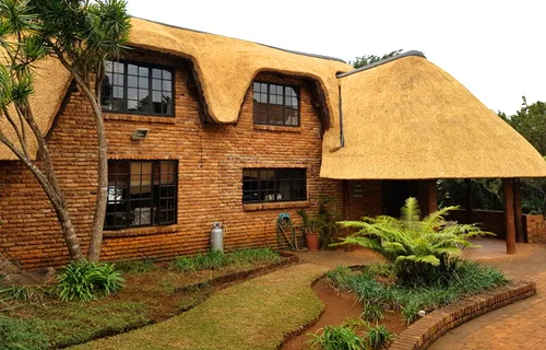 Thatched-roof venue with brick walls and green landscaping.