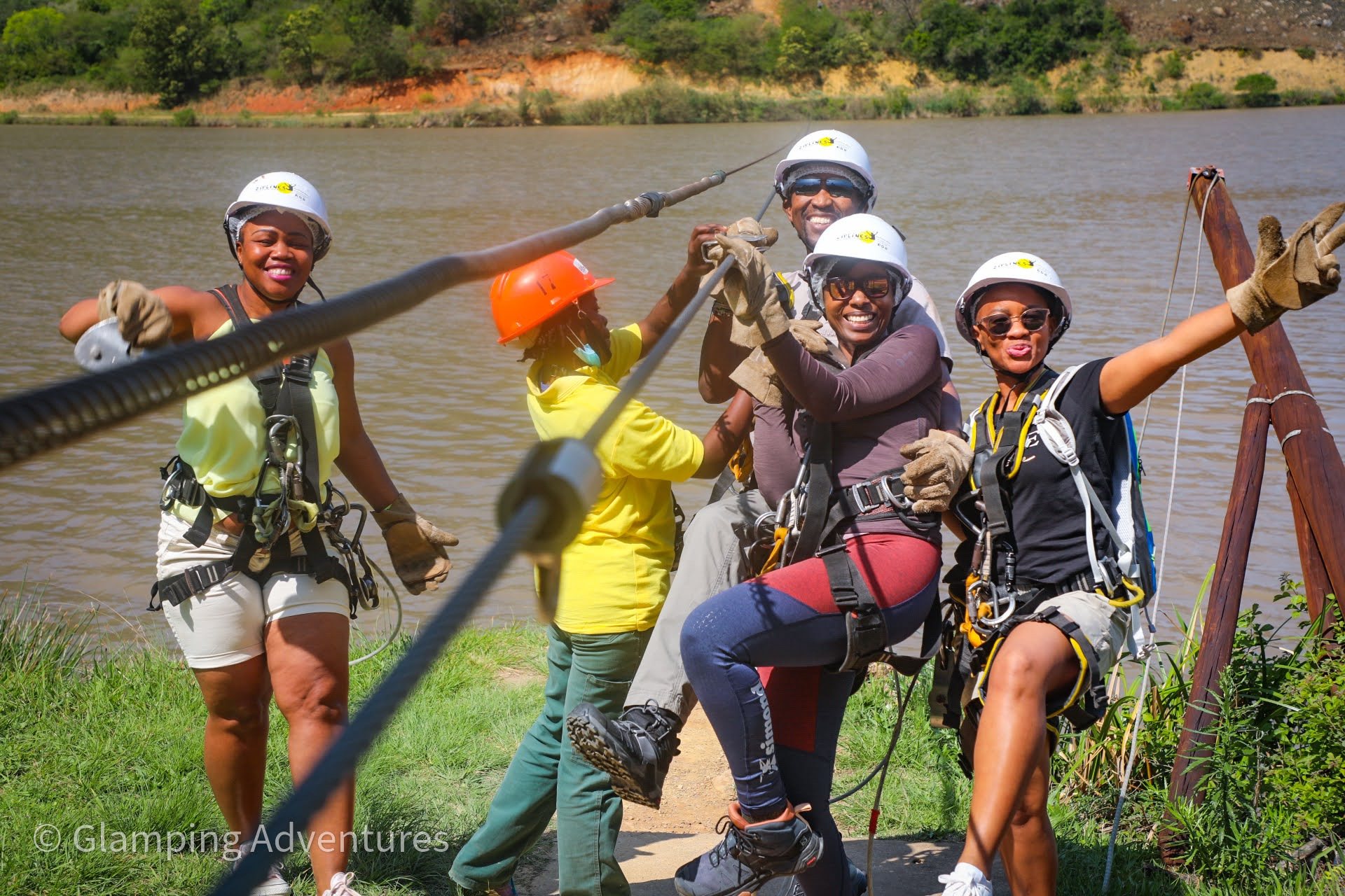 Group of five people preparing for zip-lining near a lake.