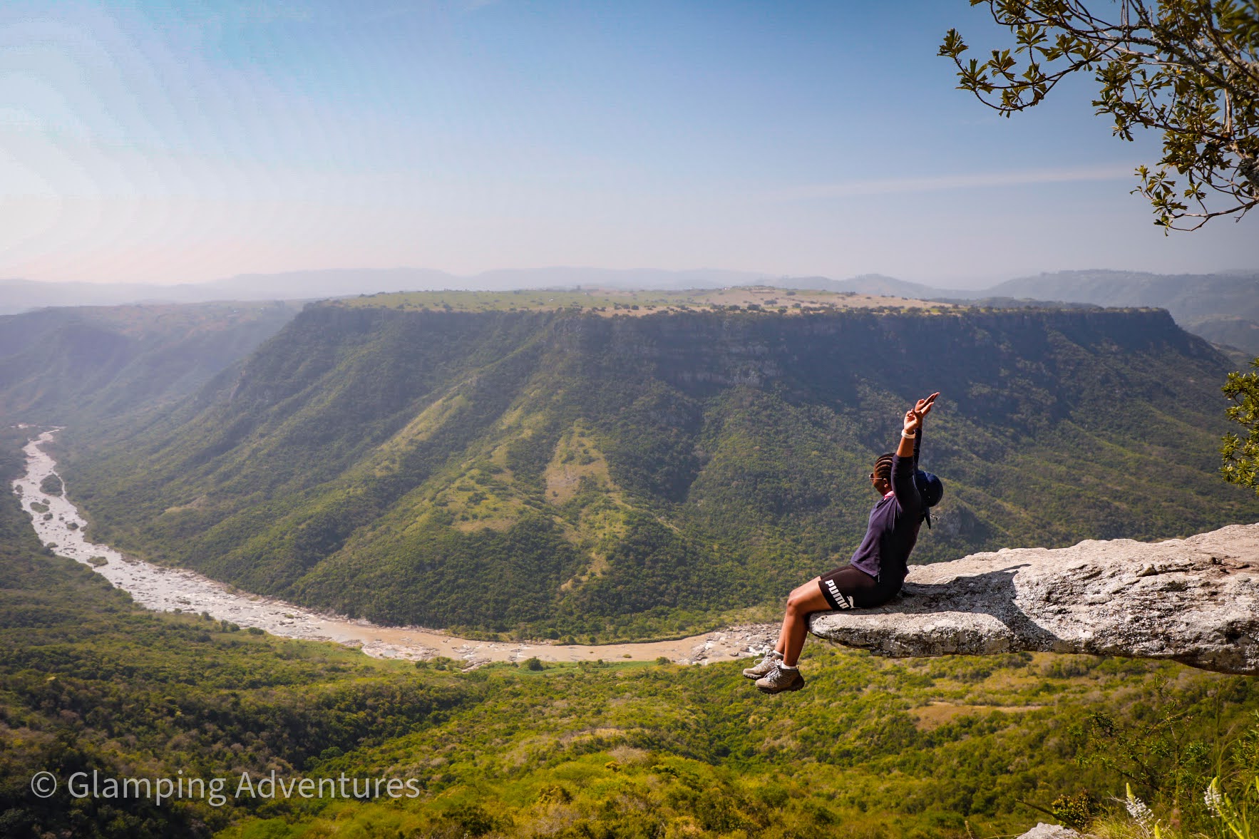 Guest sitting on a cliff overlooking a lush valley