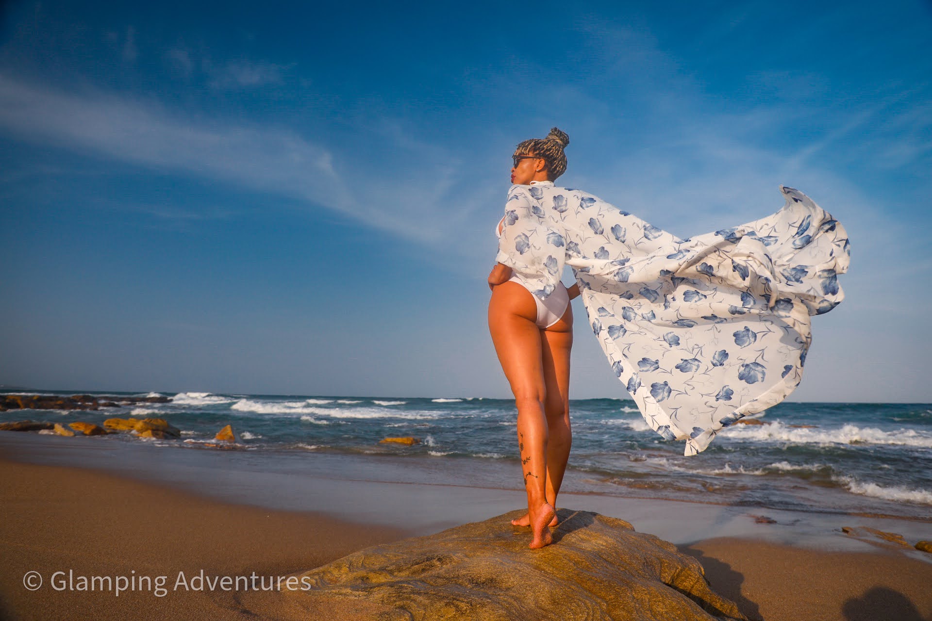 Person in a flowing garment standing on a beach near the ocean.