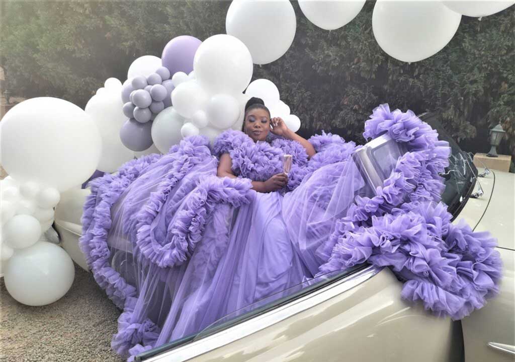 Vintage car decorated with balloons and a model in purple gown.