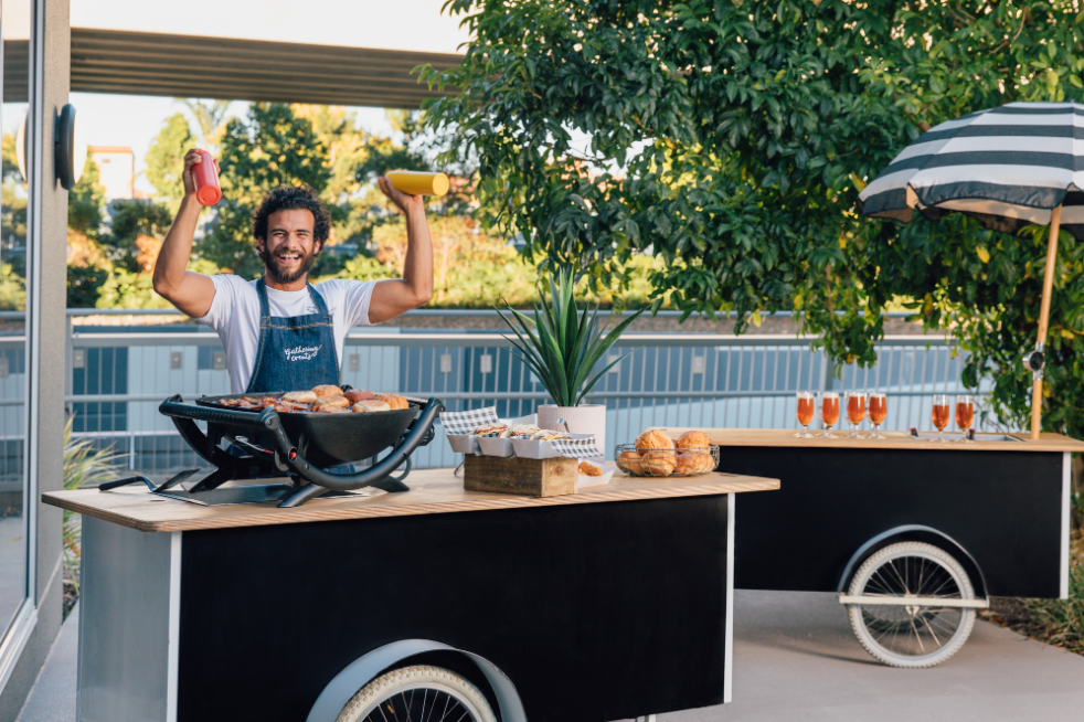 Caterer at an outdoor snack bar with grilled food.