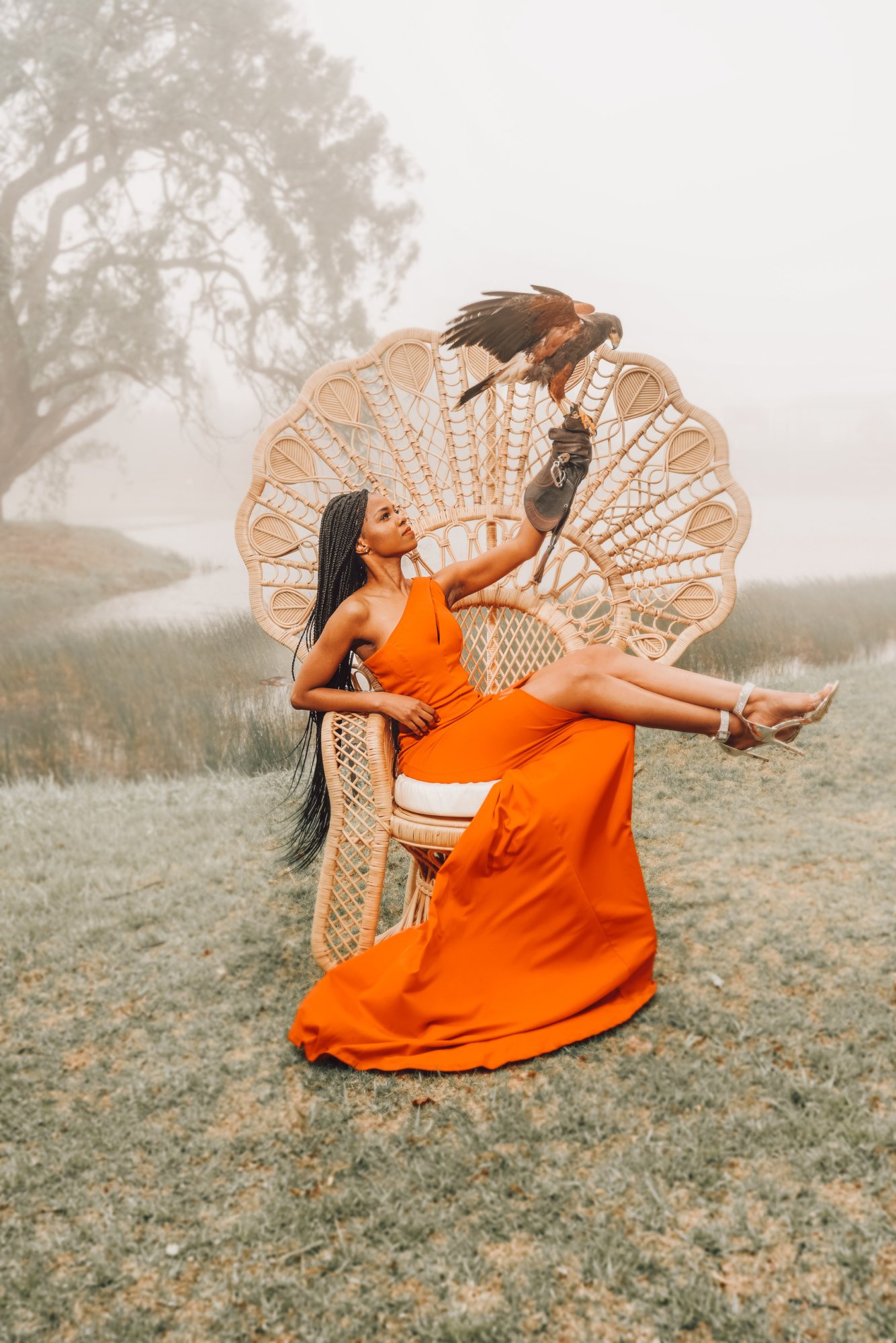 A woman in an orange dress sitting on a peacock throne chair with a bird.