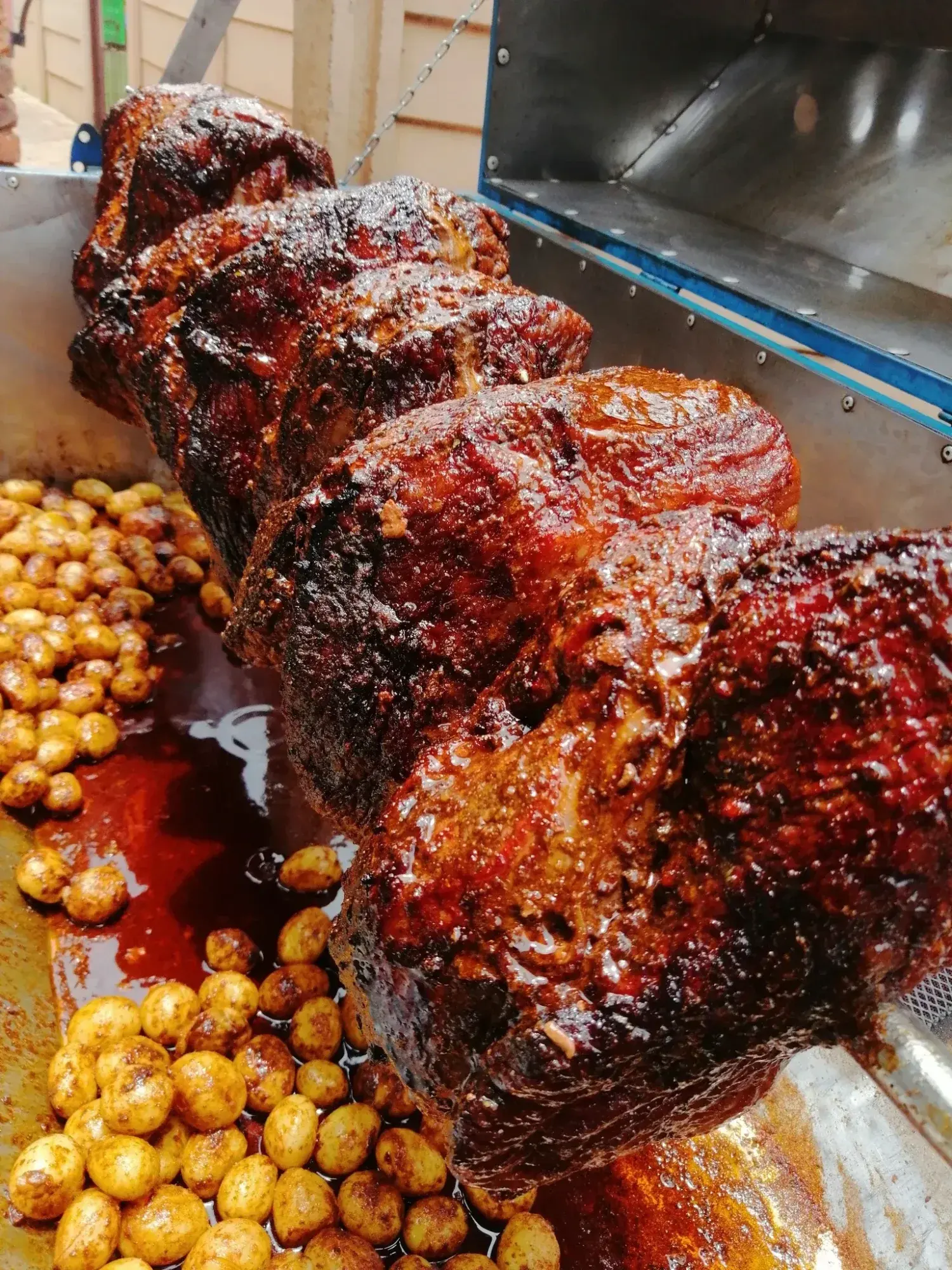 Slow-roasted meat on a spit with roasted potatoes.
