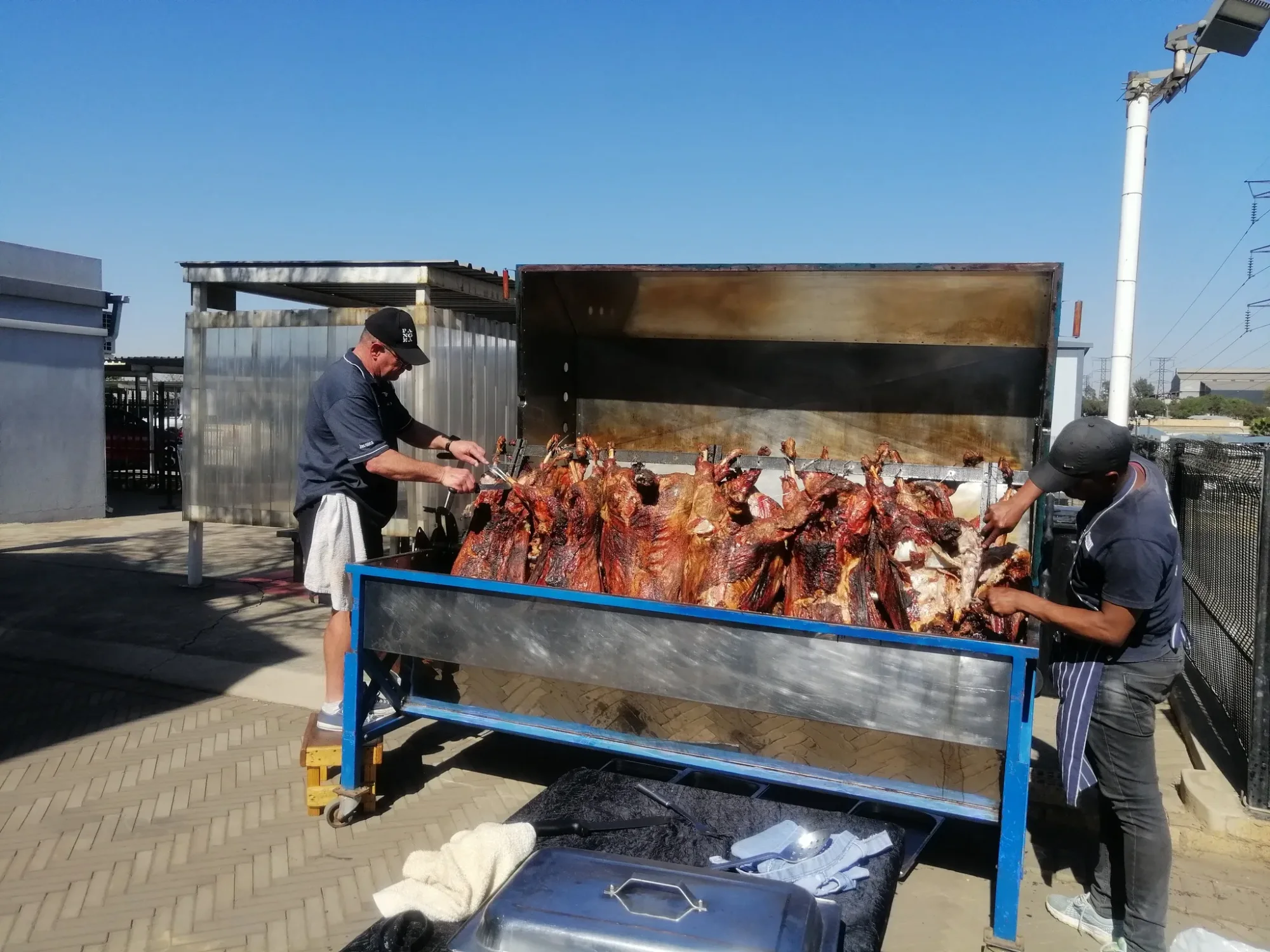 Two chefs preparing spit-roasted meats outdoors