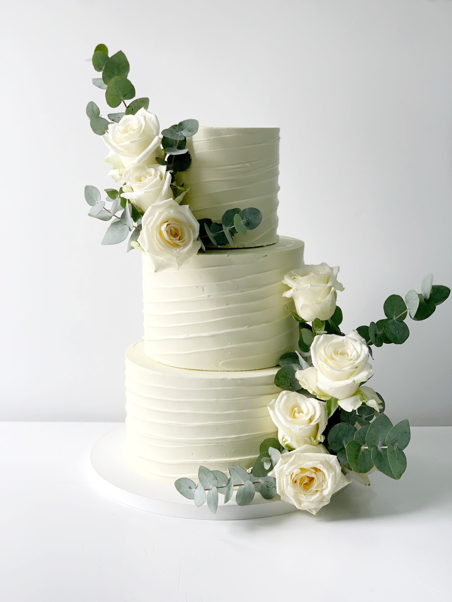 Two-tiered white wedding cake with roses and eucalyptus.