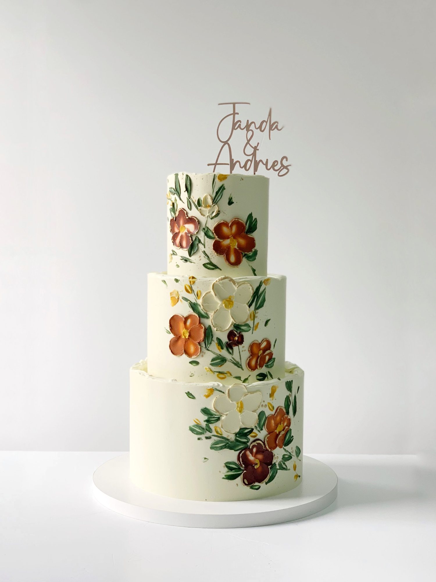 Three-tier wedding cake with floral designs and a name topper.