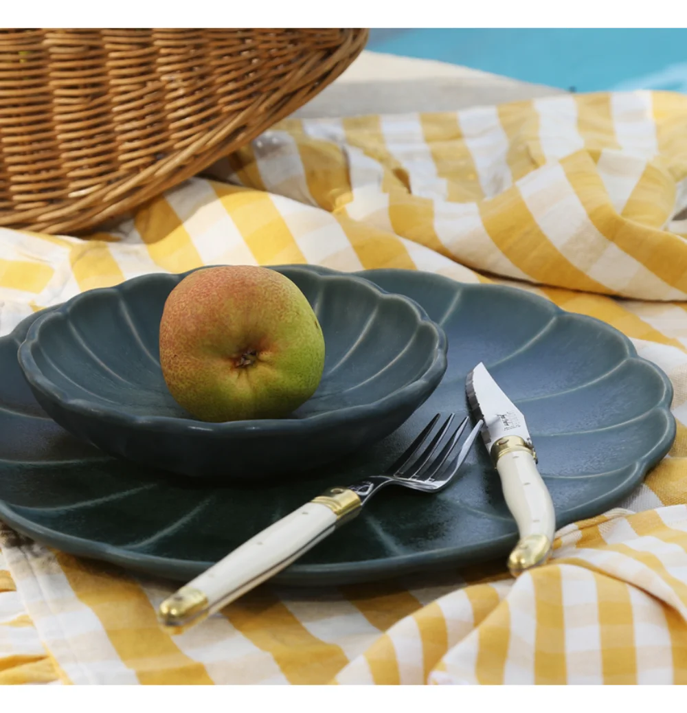 A plate with bowl, apple, fork, and knife on a checkered cloth