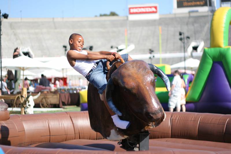 Child riding a mechanical bull at an outdoor event.