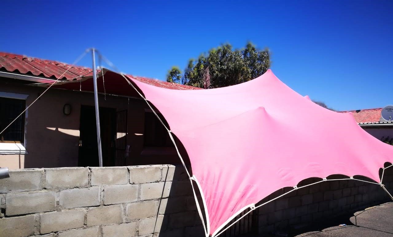 A pink stretch tent set up near a house and wall.