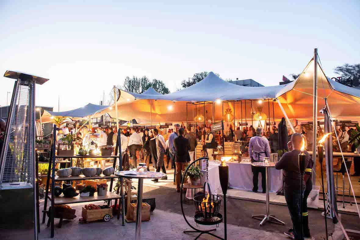 Outdoor event setup with tents, stalls, and guests socializing