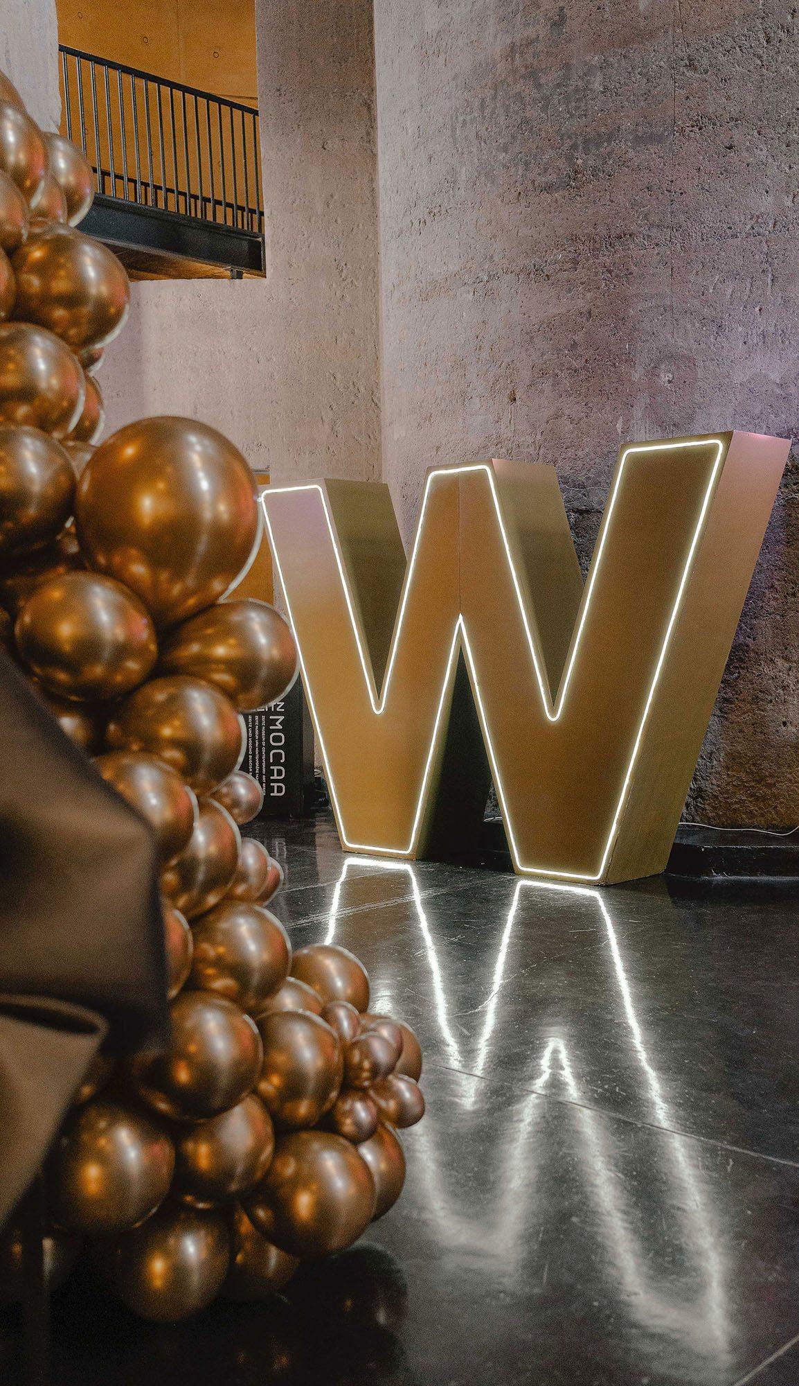 Large illuminated letter W in gold with a balloon arrangement