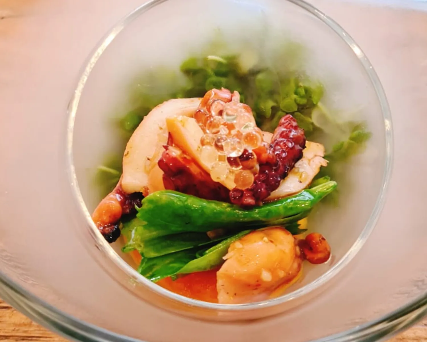 Seafood dish in a foggy glass bowl with octopus and greens.