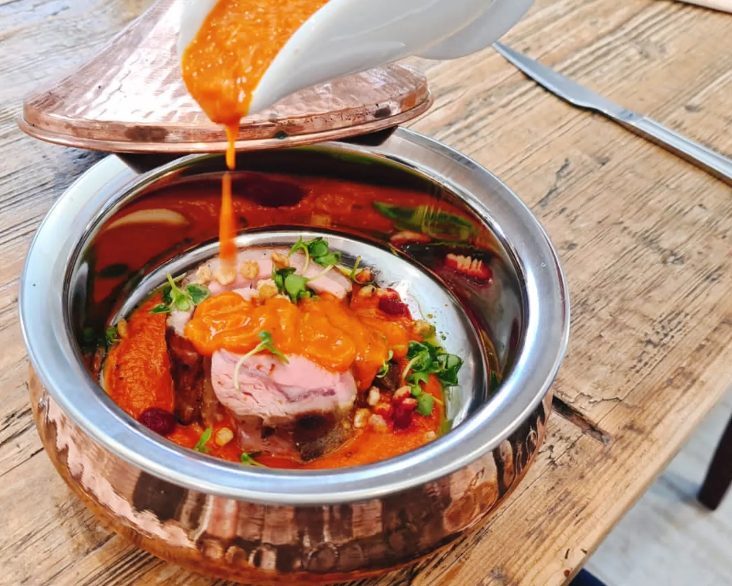 Main course with sauce being poured over meat in a copper bowl.