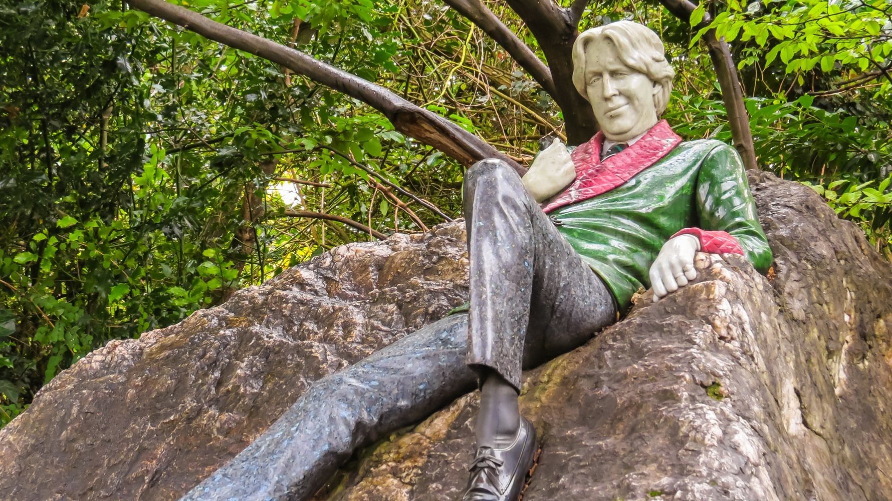 Sculpture of a man sitting on a rock surrounded by greenery.