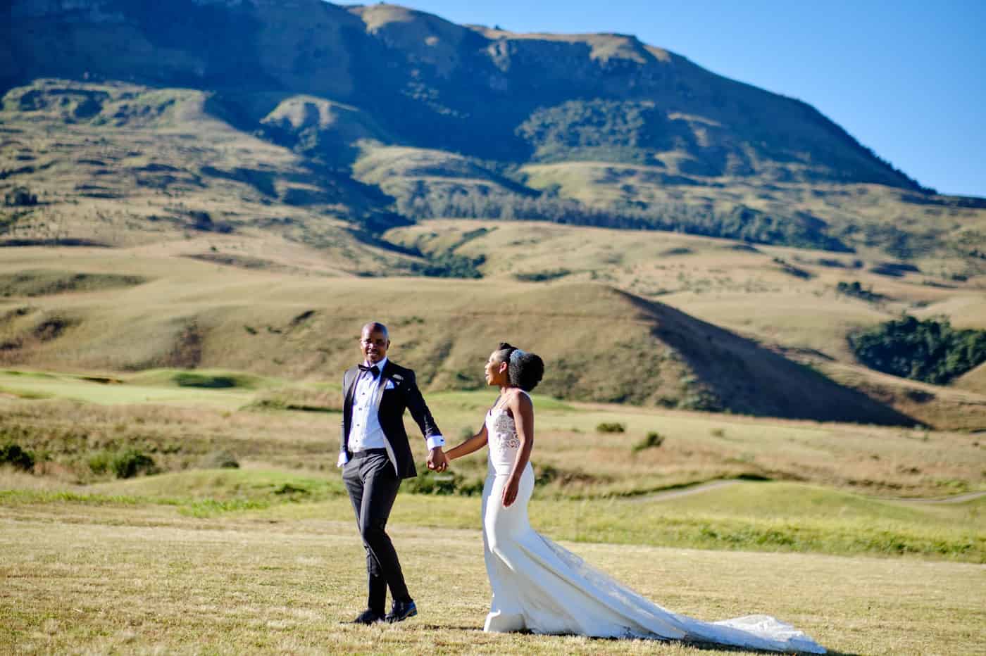 Couple walking in a green field with mountains in the background